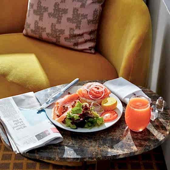 A smoked salmon bagel breakfast with grapefruit juice and a newspaper on a small seating area in a room at Park Lane New York.