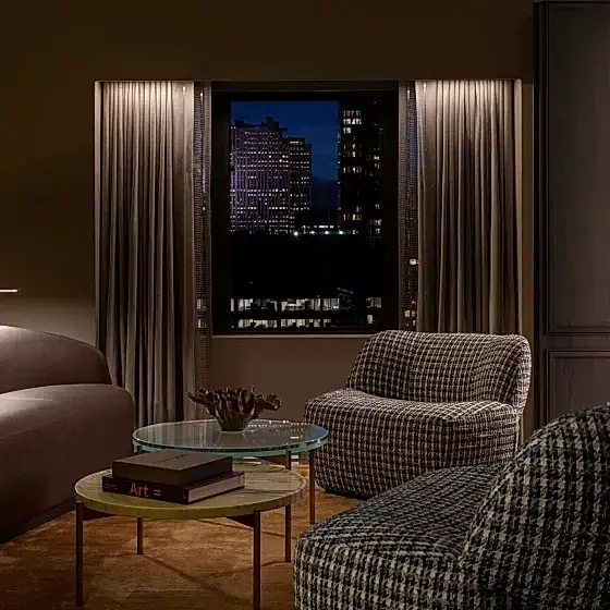 A seating area with two checkered chairs, brown leather sofa and tiered table in the Belvedere Suite at Park Lane New York.