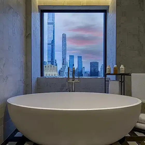 A deep bathtub beneath a window overlooking the New York city skyline in the Conservatory Suite at Park Lane New York.