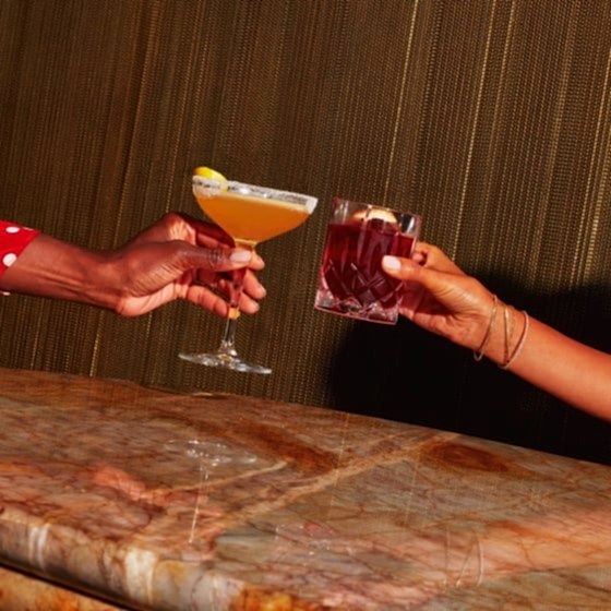 Two women clinking two cocktails together.