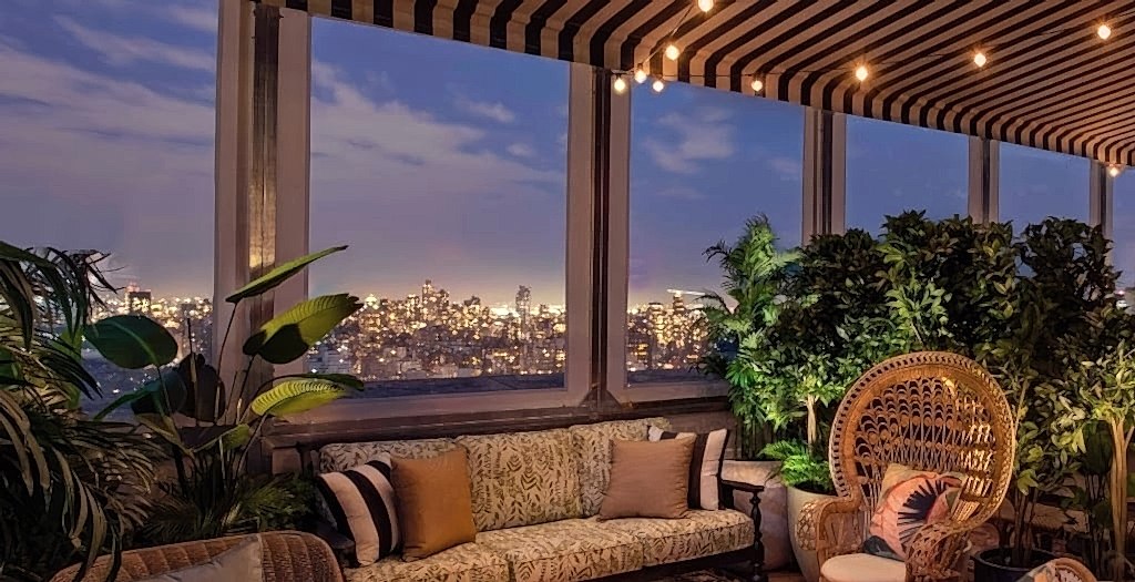 A cozy lounge area with warm lighting at dusk, New York City skyline in the background.