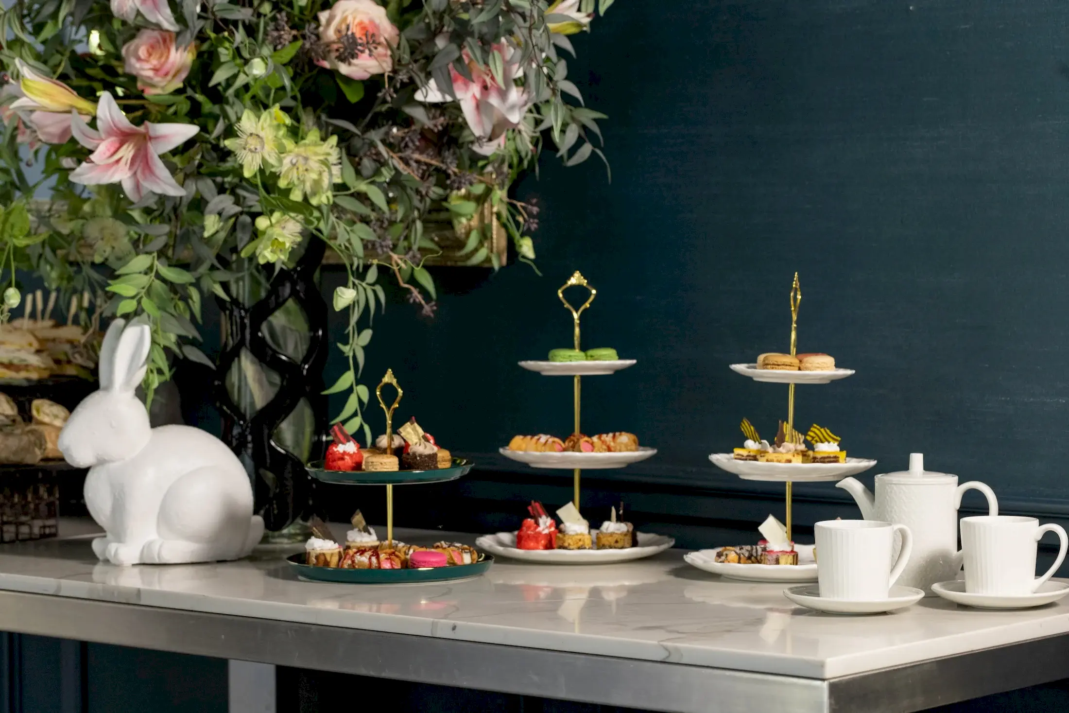Three tiered trays of desserts on a table with a large bouquet of flowers.