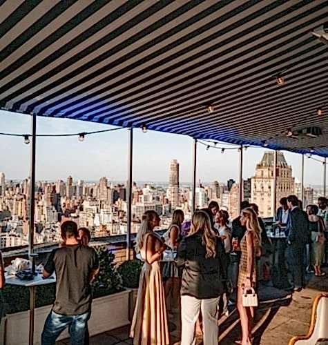 An event space with a view of New York City full of people mingling.