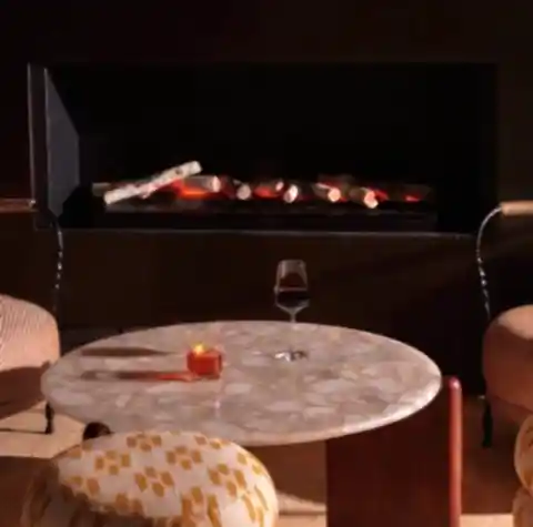 A glass of wine and a cocktail on a table in front of a fireplace.